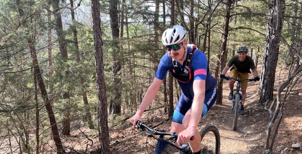 Two mountain bikers riding toward the camera on a trail through pine woods
