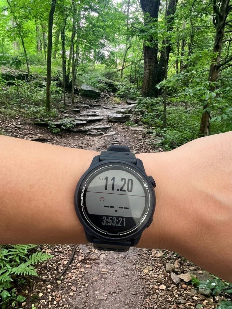 A GPS watch on a wrist, held over a rocky trail