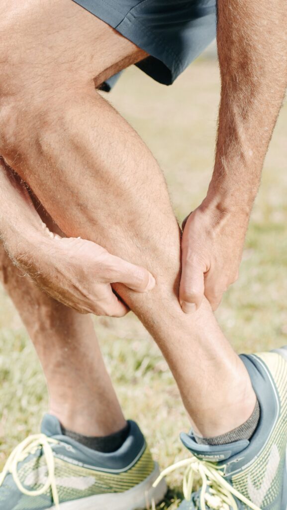 A person in running shoes holds a sore calf with both hands