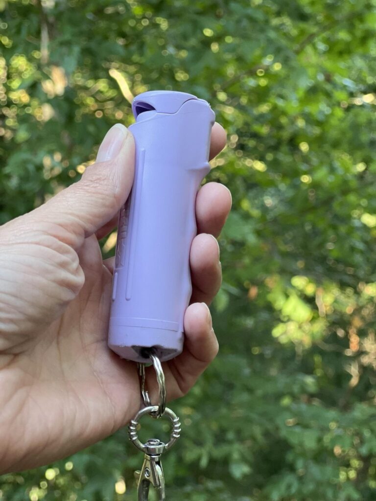 A hand holding a small purple canister of pepper gel on a key ring