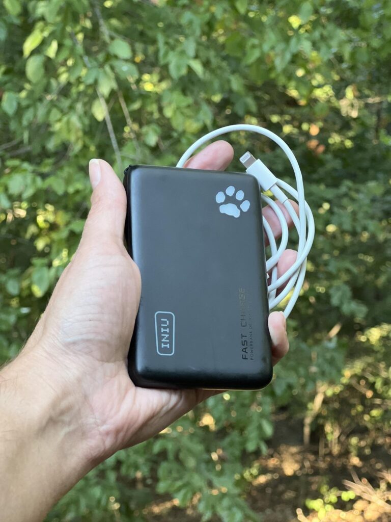 A hand holding a portable phone charging brick with a cable