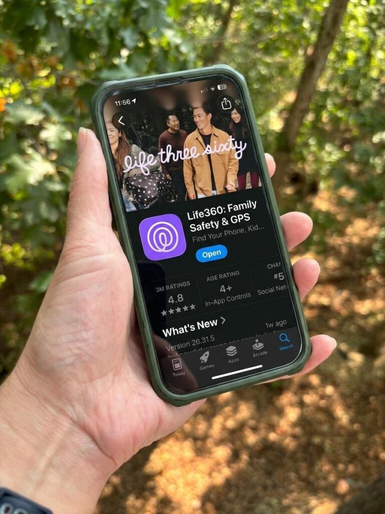 A hand holding a phone open to the app store page for the Life360 location sharing app, with woods behind