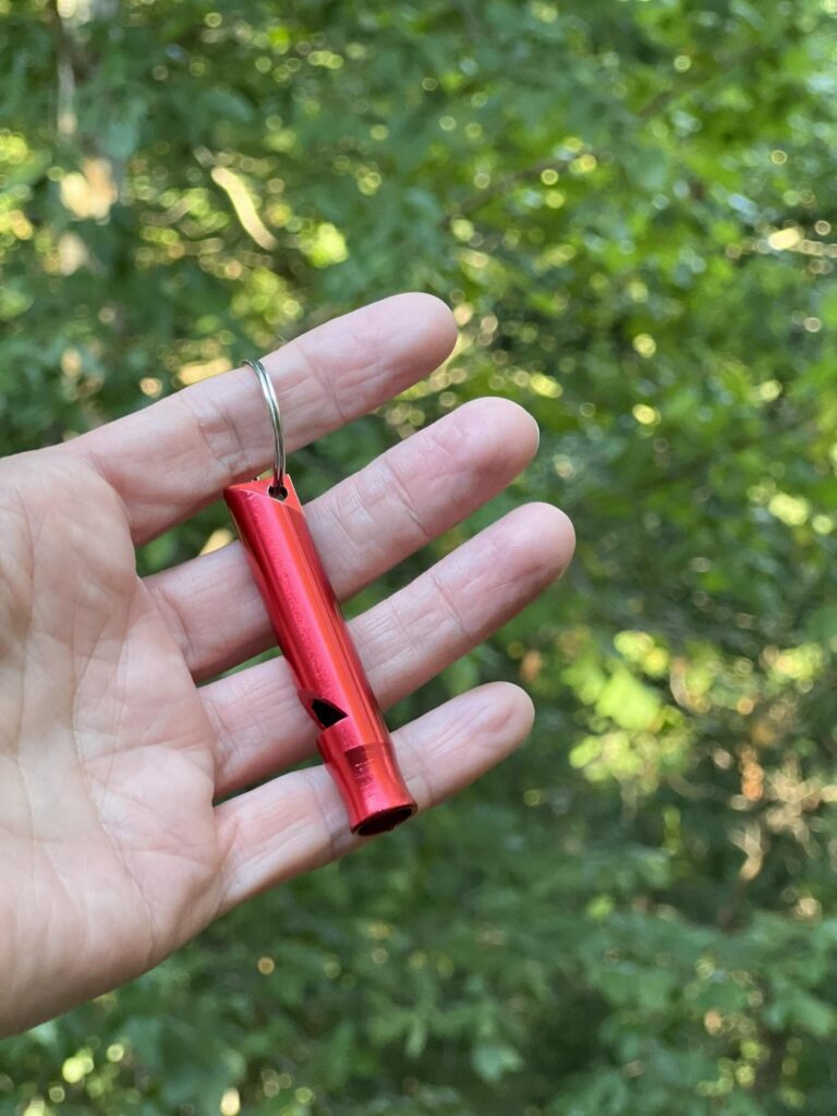 A hand holding a red whistle on a key ring