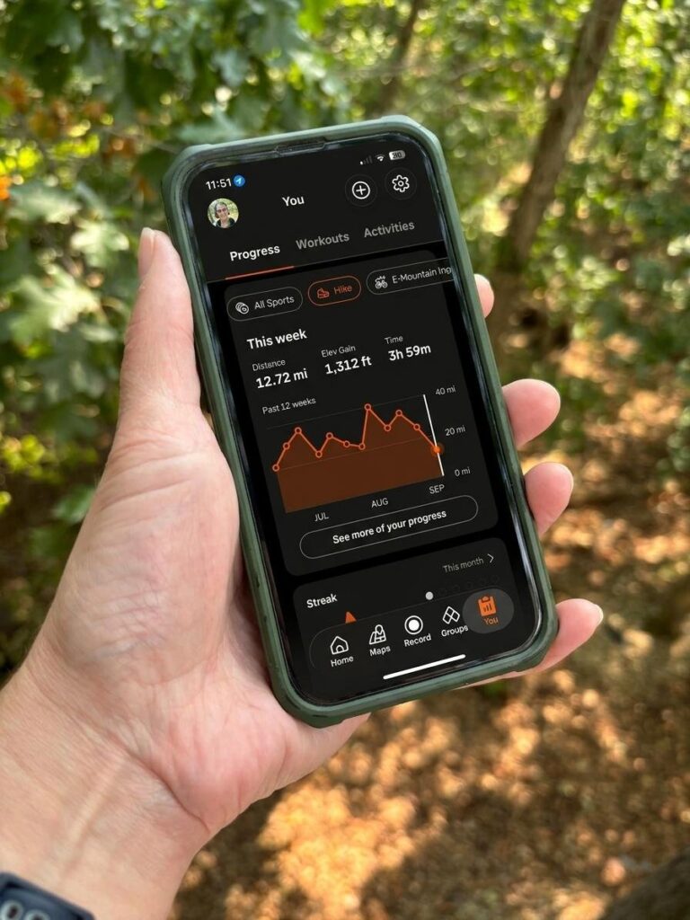 A hand holding a phone showing hiking stats in the Strava app